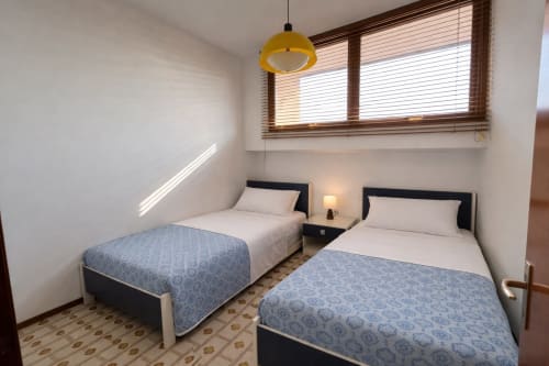 Twin bedroom in Villa Loris apartment at Anthea hotel, Lignano Sabbiadoro, with blue patterned bedspreads and yellow pendant