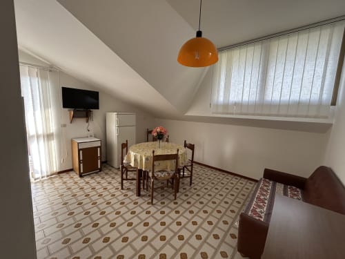Anthea hotel apartment Villa Loris in Lignano Sabbiadoro features dining area with round table, orange pendant lamp, TV, and