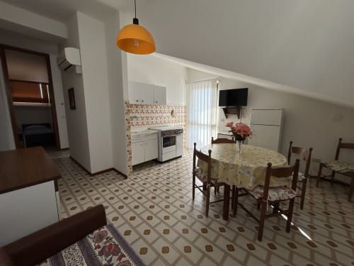 Villa Loris apartment dining area with kitchen, orange pendant light, and garden views at Anthea hotel in Lignano Sabbiadoro