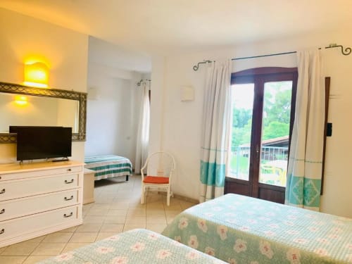 Bright hotel room at Domu Incantada with twin beds, garden view balcony, TV, and modern amenities in Muravera
