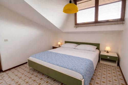 Modern bedroom with green bed frame, blue bedding, yellow pendant lamp, and skylight windows at Anthea Hotel in Lignano