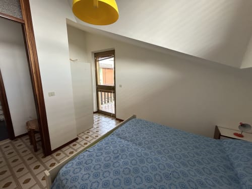 Bedroom at Anthea Hotel in Lignano Sabbiadoro with blue patterned bedspread, yellow pendant light, and balcony access