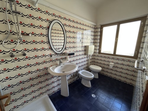 Bathroom at Anthea Hotel Lignano Sabbiadoro featuring vintage patterned wallpaper, white fixtures, dark tile floor