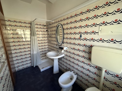 Vintage bathroom at Anthea Hotel, Lignano Sabbiadoro, with retro red and navy tile pattern and pedestal sink