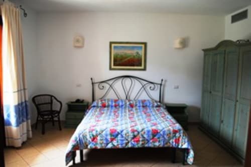 Camera luminosa all'Hotel Domu Incantada di Muravera con letto ornato, biancheria colorata, armadio e vista sul giardino.