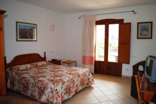 Spaziosa camera da letto all'Hotel Domu Incantada con letto in legno, balcone con vista giardino e servizi moderni a Muravera