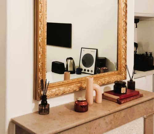 Elegant vanity with ornate gold mirror, diffusers, candles, and red books in Paris apartment at Conciergerie Saint Martin
