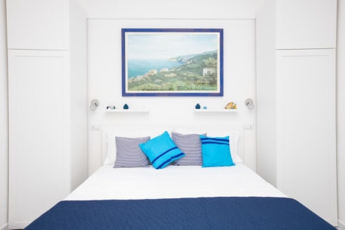 Camera luminosa negli Appartamenti Momi a Sorrento con vista costiera incorniciata in blu sopra il letto