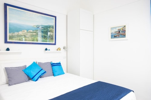 Camera luminosa di Appartamenti Momi a Sorrento con opere d'arte costiera, accenti blu e cuscini a righe