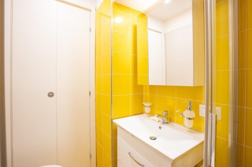 Bagno moderno con piastrelle gialle vivaci, lavabo bianco e box doccia in vetro presso Appartamenti Momi, Sorrento