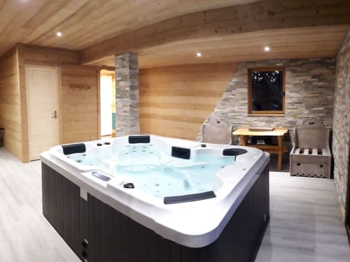 Bain à remous luxueux dans un spa aux panneaux de bois, Chalets Cocody à Jausiers, avec accents de pierre et décor de chalet montagnard