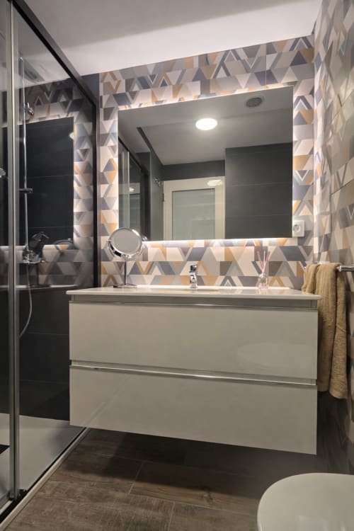Modern bathroom with white vanity, geometric tiled walls, illuminated mirror, and glass shower enclosure at La Aldea vacation