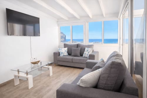 Modern apartment living room with sea view in La Aldea, gray sofas, TV, large windows overlooking ocean and coastline