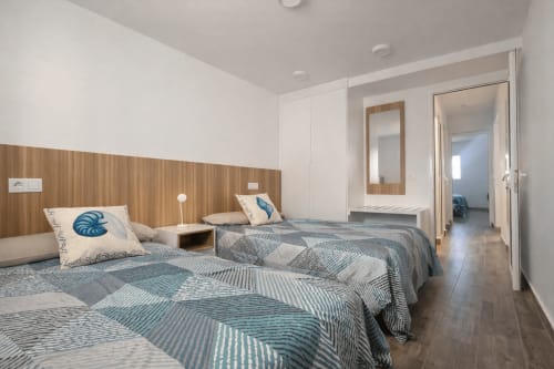 Modern bedroom in La Aldea apartment with two beds, wood headboard, blue patterned bedding, and en-suite bathroom access