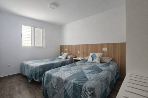 Twin bedroom with wood headboard, blue patterned bedspreads, and window at Apartamento Severo 3 in La Aldea, Spain