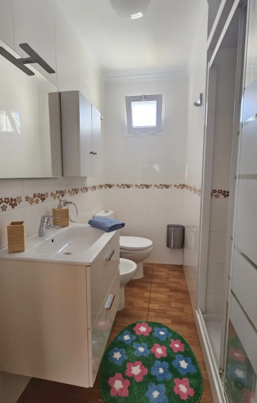 Modern bathroom in Apartamento Galoponte, La Aldea de San Nicolas with white tiles, wooden vanity, and flower-patterned mat
