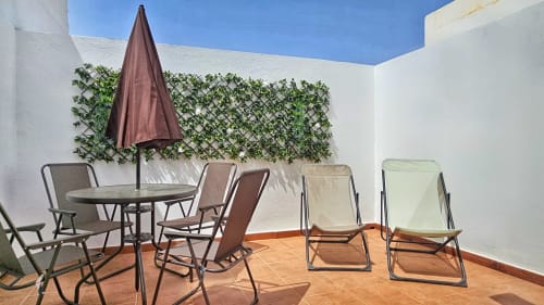 Sunny terrace with dining table, lounge chairs, umbrella, and green lattice wall at Alojamientos vacacionales en La Aldea