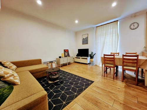 Sala de estar de apartamento moderno em Lisboa com sofá marrom, TV, zona de refeições, piso de madeira e grandes janelas