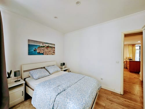 Quarto luminoso no Lisbon Village Apartments com roupa de cama azul estampada, cabeceira branca, pisos em madeira e arte costeira