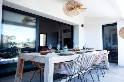 Modern dining area at Locavilla villa with whitewashed table, woven chairs, and pool view through glass doors in Colombes
