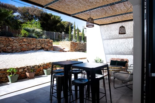 Modern covered patio at Locavilla villa with black dining table, hanging lights, and stone walls overlooking garden in