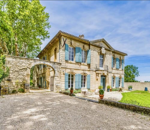 Villa en pierre aux volets bleus et portail à arc dans les jardins de Provence à Arles