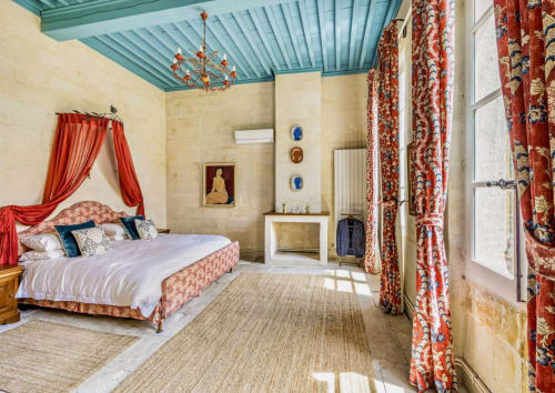 Chambre luxueuse à la Conciergerie Maurin à Arles avec lit à baldaquin, rideaux rouges, plafond turquoise et vue sur jardin