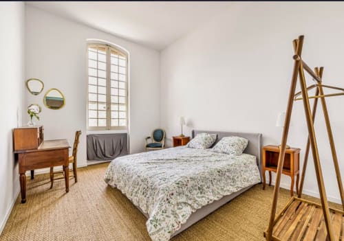 Chambre lumineuse à la Conciergerie Maurin d'Arles avec parure florale, mobilier en bois et vue sur le jardin par de grandes fenêtres
