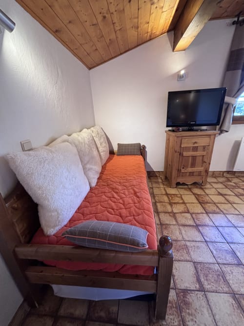 Cozy studio bedroom at Chez Francine with wooden bed, red bedding, white pillows, TV, and wooden furniture in Notre Dame de
