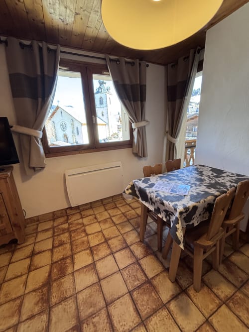 Studio Aravis dining area at Chez Francine with church views through windows, wooden furniture, and terracotta tile flooring