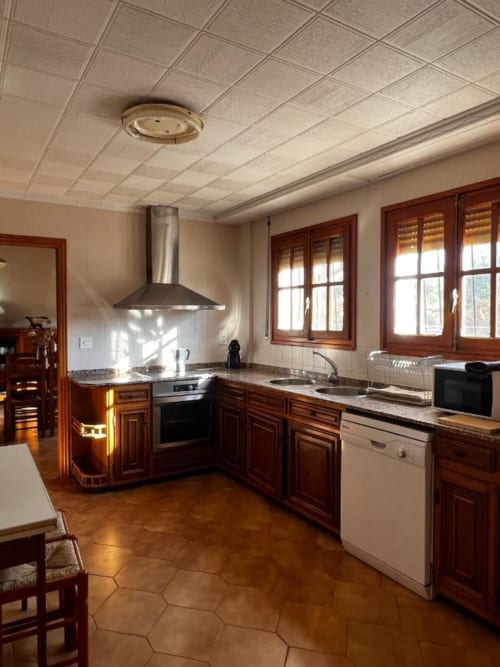 Cocina moderna con muebles de madera, electrodomésticos de acero inoxidable y suelos de baldosa en Casa Rural Finca El Olivar
