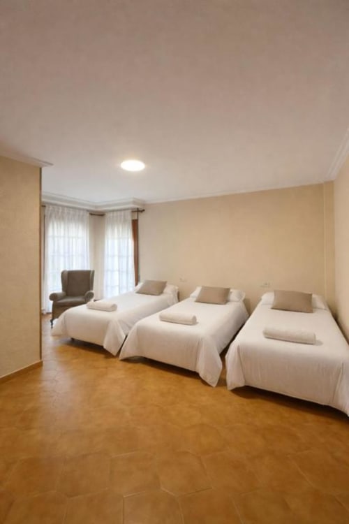Amplio dormitorio en villa Casa Rural Finca El Olivar con tres camas, paredes amarillas, suelo de madera y terraza con vista al jardín