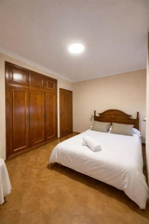 Dormitorio espacioso en Casa Rural Finca El Olivar con cama de madera, armario y suelo de barro cocido