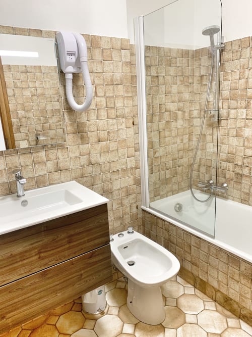 Modern bathroom at Chez Francine with beige tiles, sink, bidet, shower enclosure, and wooden vanity