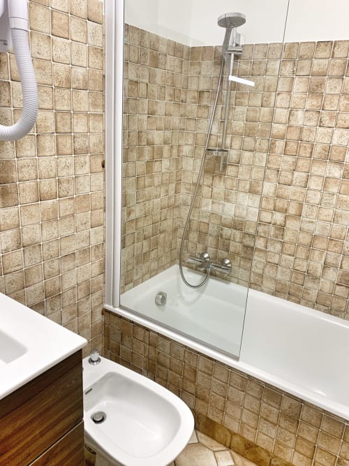 Modern bathroom at Chez Francine studio apartment with beige tile walls, glass shower enclosure, white fixtures, and wood