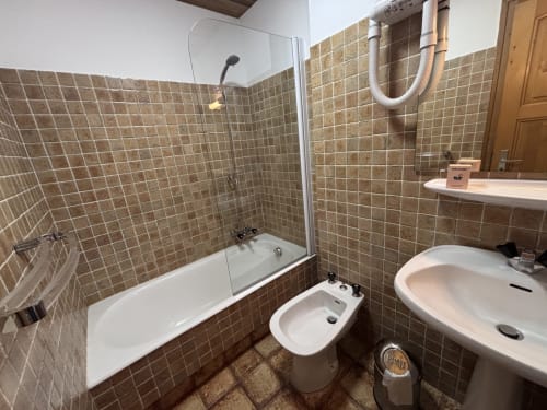Bathroom at Chez Francine studio apartment with brown tile walls, bathtub, bidet, sink, and shower fixtures
