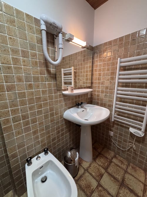 Compact bathroom at Chez Francine studio with tiled walls, pedestal sink, toilet, heated towel rack, and wall-mounted mirror