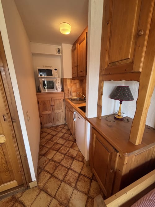 Cozy studio kitchen at Chez Francine with wooden cabinets, tile floor, and warm lighting in Notre Dame de Bellecombe
