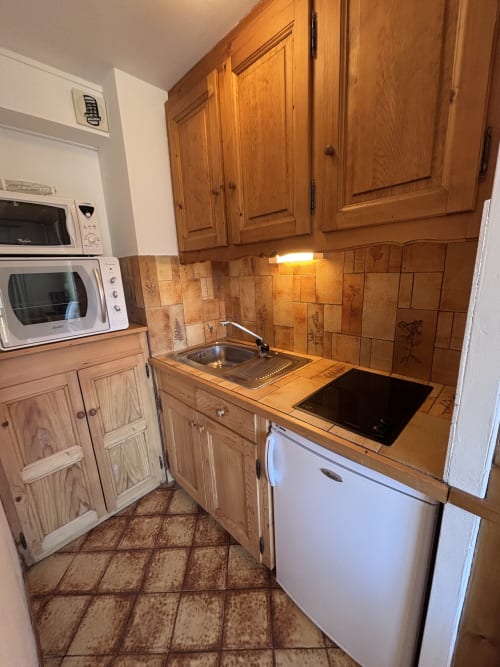 Compact kitchen in Studio Ban rouge at Chez Francine with wooden cabinets, tiled backsplash, and stainless steel appliances