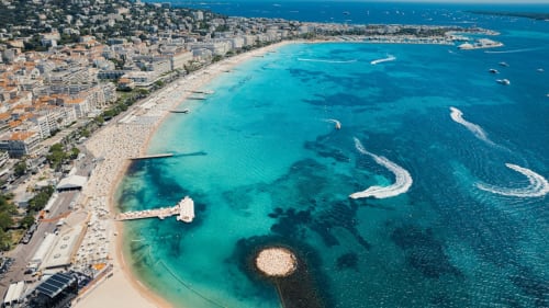 Straordinaria spiaggia mediterranea con acque turchesi, sabbia dorata e edifici costieri sullo sfondo
