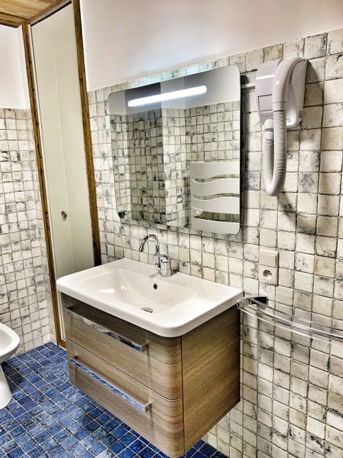 Modern bathroom with white sink, wood vanity, illuminated mirror, and vintage cream tile walls at Chez Francine, Notre Dame