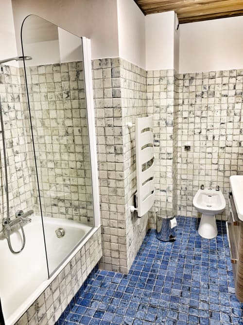 Modern bathroom in Chez Francine apartment with cream and blue tiled walls, shower, toilet, and heated towel rack.