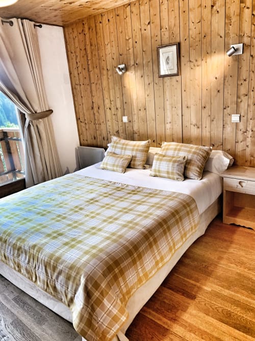 Cozy wood-paneled bedroom in Chez Francine apartment with plaid bedding, mountain view window, and rustic alpine décor