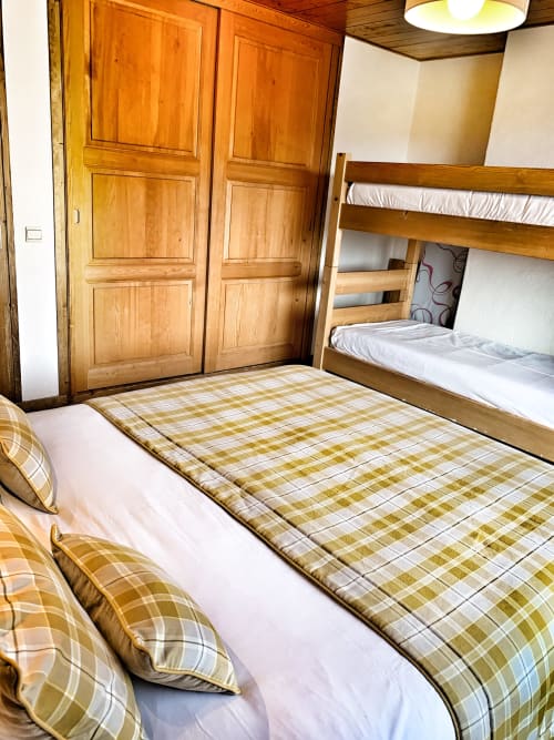 Cozy bedroom at Chez Francine in Notre Dame de Bellecombe with wooden bunk bed, plaid bedding, wardrobe, and mountain views
