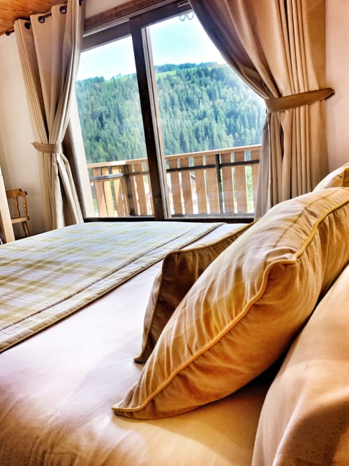 Spacious bedroom at Chez Francine with beds, beige curtains, wooden balcony railing, and mountain forest views in Notre Dame