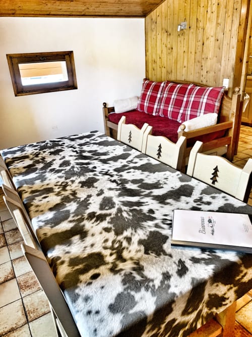 Cozy alpine bedroom at Chez Francine with cow-print bedding, red plaid sofa, wood-beamed ceiling, and mountain views in Notre