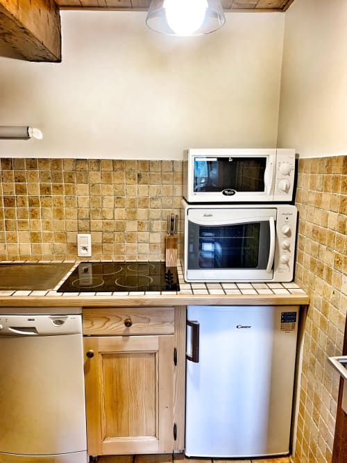 Compact kitchen in Chez Francine apartment with stove, microwave, small refrigerator, and tiled backsplash in Notre Dame de