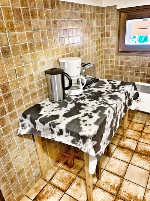 Kitchenette in Chez Francine apartment with coffee maker, kettle, and cow-print tablecloth on wooden table