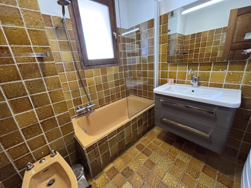 Modern bathroom at Chez Francine apartment with golden tile walls, white sink, bathtub and shower in Notre Dame de Bellecombe