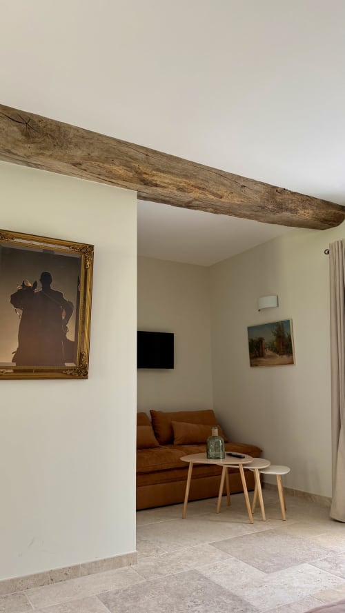 Chambre Vénerie du Cloffy B&B avec poutres apparentes, canapé en cuir marron, portrait encadré et vue sur le jardin